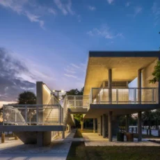 Modern concrete pavilion with an elevated walkway and stairs, by the water at sunset.