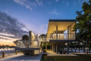 Modern concrete pavilion with an elevated walkway and stairs, by the water at sunset.